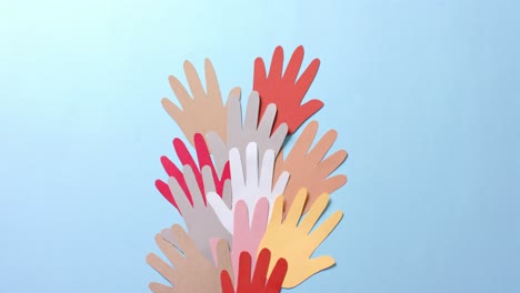 close up of hands together made of colourful paper on blue background with copy space