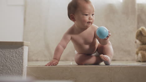 a little asian baby catching and grabbing a ball and throwing it again