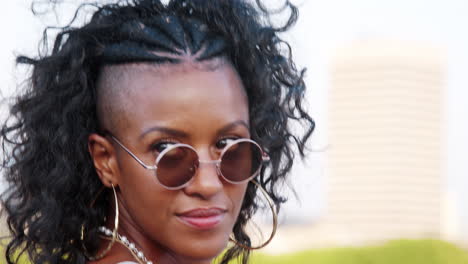joven negra de moda en camisola y gafas de sol caminando por el puente, mirando hacia atrás y riendo a la cámara, cerca, seguir el tiro