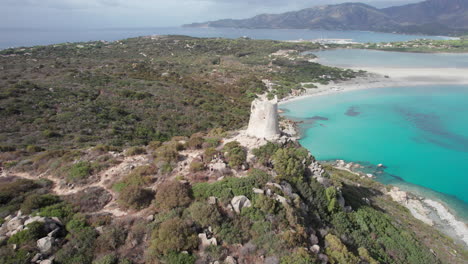 Torre-di-Porto-Giunco,-Sardinia:-aerial-view-in-orbit-and-close-to-the-Torre-di-Porto-Giunco-at-Cape-Carbonara-and-the-turquoise-color-of-the-sea