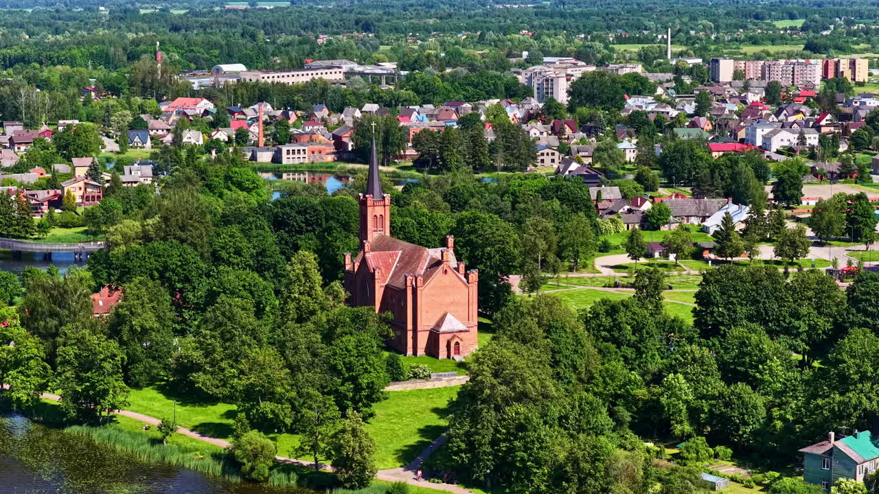Slow aerial parallax movement reveals Biržai Evangelical Reformed Church nestled in lush greenery and parkland in Lithuania