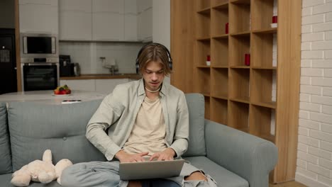 Young-man-in-headphones-make-video-call-using-laptop-sitting-at-home