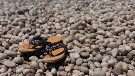 Flip-flops-washing-by-sea-flows-of-clean-transparent-water-on-pebbles-beach,-vacation-concept