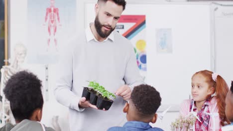 diverse male teacher and happy schoolchildren studying plants in school classroom