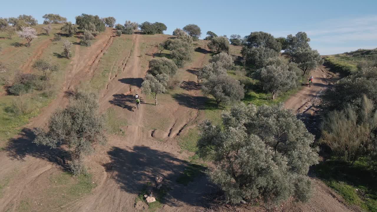 amplia toma aérea mientras un piloto de motocross realiza un truco peligroso sobre una colina en una polvorienta pista de motocross rodeada de árboles en málaga, españa