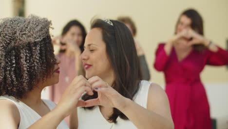 primer plano de felices lesbianas recién casadas mostrando el corazón con las manos, besándose y mirando a la cámara