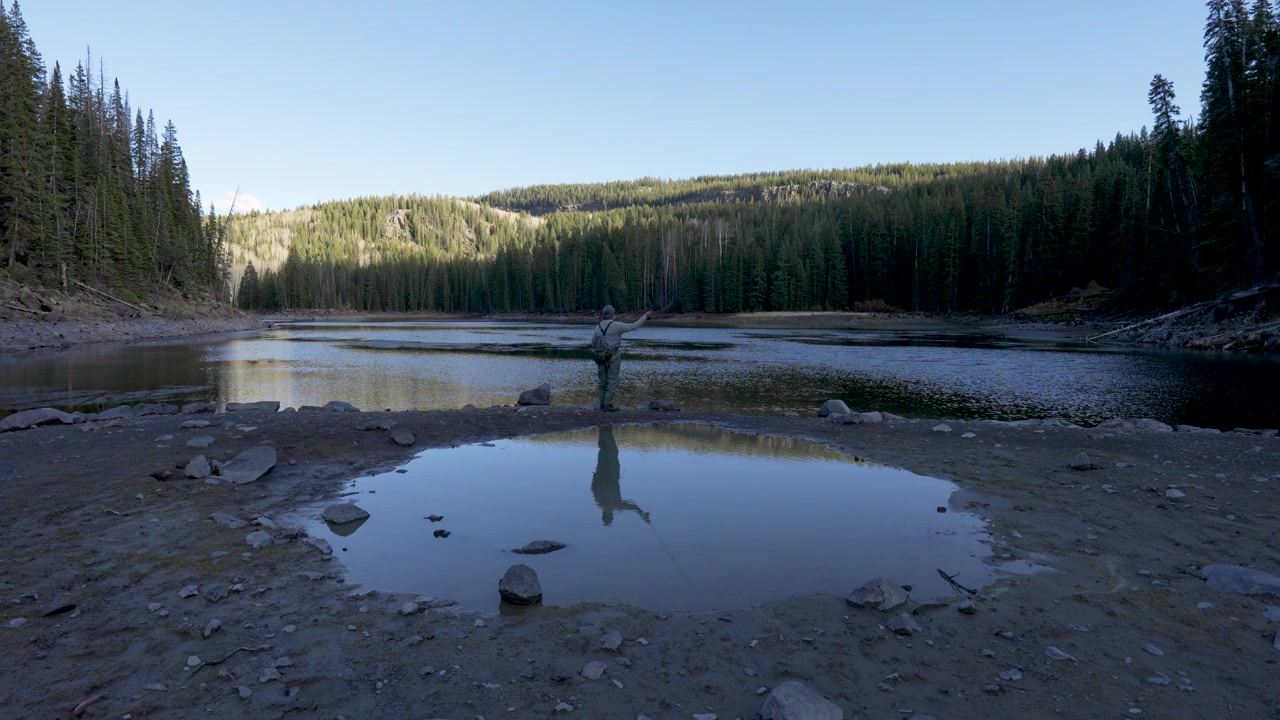Stille vidvinkeloptagelse fra jorden af en enlig fisker, der kaster ud ved en stille alpesø på Colorados Grand Mesa, fisker efter regnbueørred og bækørred i Rocky Mountains