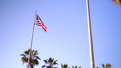 Flagge-Der-Vereinigten-Staaten-Weht,-Im-Hintergrund-Ein-Blauer-Himmel-Und-Palmen