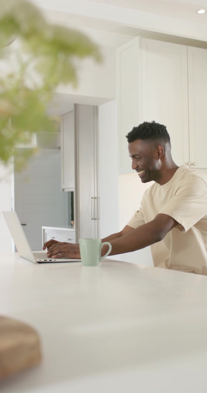 Vertical video: African American man seeing email, typing on laptop at kitchen island, copy space