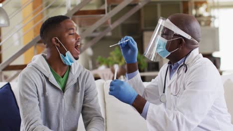 Médico-Senior-Afroamericano-Que-Realiza-Una-Prueba-De-Covid-A-Un-Paciente-Masculino-En-Casa,-Usando-Máscaras-Faciales