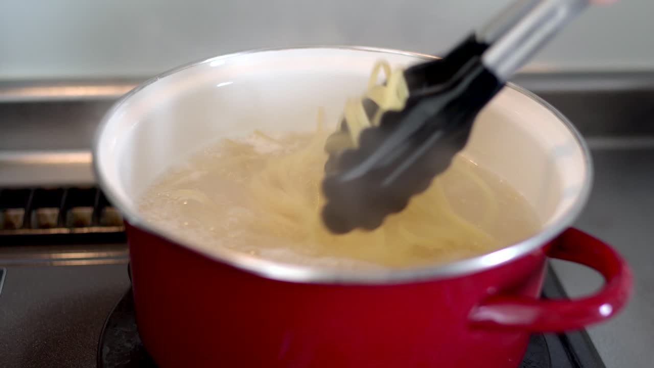 cocinar pasta en una olla roja con agua hirviendo usando pinzas - primer plano