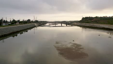 Aerial-drone-shot-starts-at-the-water-level-and-rises-up-to-reveal-the-cityscape-on-either-side-of-the-river-bed