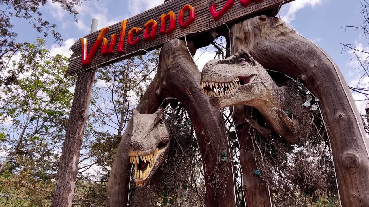 A sign above the entrance to an amusement park with dummies of prehistoric dinosaurs, the animals click their teeth, open their scary mouths
