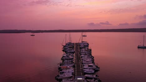 Vista-Aérea-De-Barcos-En-Un-Muelle-Con-Una-Hermosa-Puesta-De-Sol,-Siguiendo-Una-Toma-Amplia