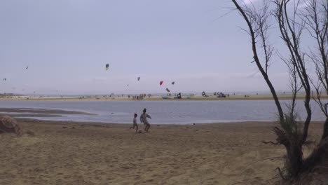 Brüder-Spielen-Fußball-Am-Strand-Und-Kiteboarder-Im-Hintergrund