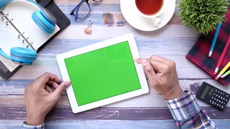 persona usando una tableta con pantalla verde en un escritorio de madera
