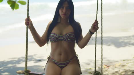 a woman in a bikini enjoys a swing on the beach with ocean waves in the background