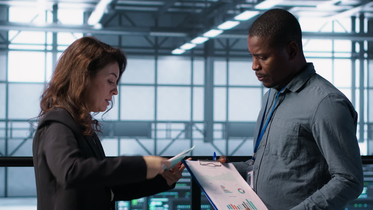 Data center team examines paperwork files in server room, reviewing system