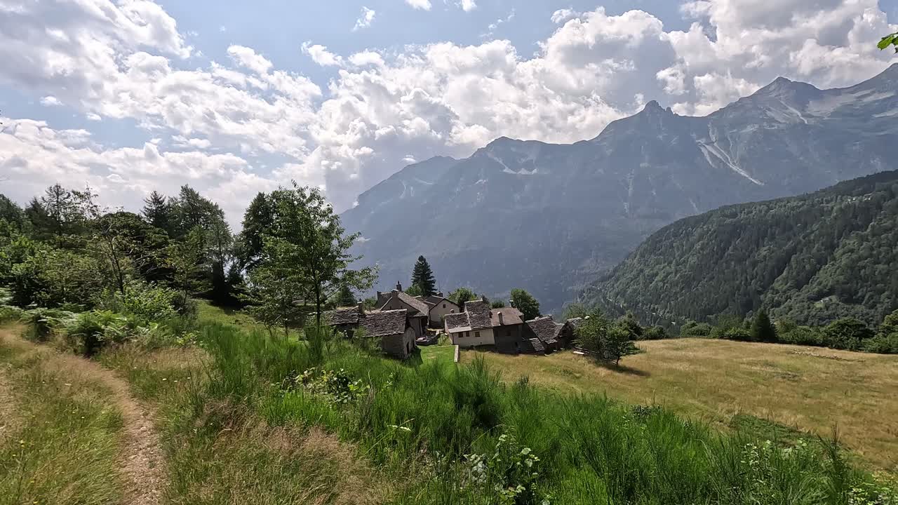 Traditional stone-roofed village near Varzo surrounded by alpine meadows, forests, and dramatic mountain peaks