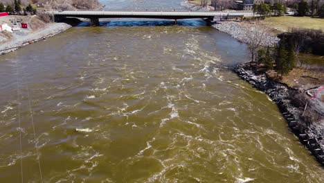 Tiro-Cercano-Del-Dron-Del-Río-Ottawa-En-Primavera-Inclinándose-Hacia-Los-Edificios-Del-Parlamento-En-La-Distancia