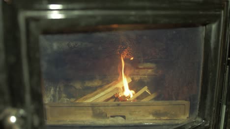 man lighting fire adding kindling to wood burning stove