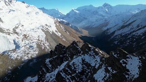 aerial snowy winter mountain range ridgeline with steep valleys below on sunny day, flying around peaks