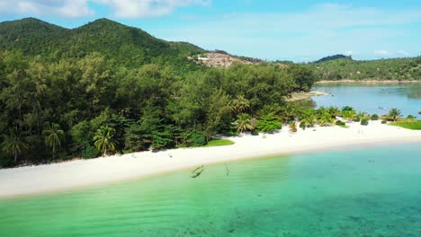 Peaceful-shoreline-of-tropical-island-with-calm-turquoise-lagoon,-white-sandy-beach-and-palm-trees-forest-in-Thailand