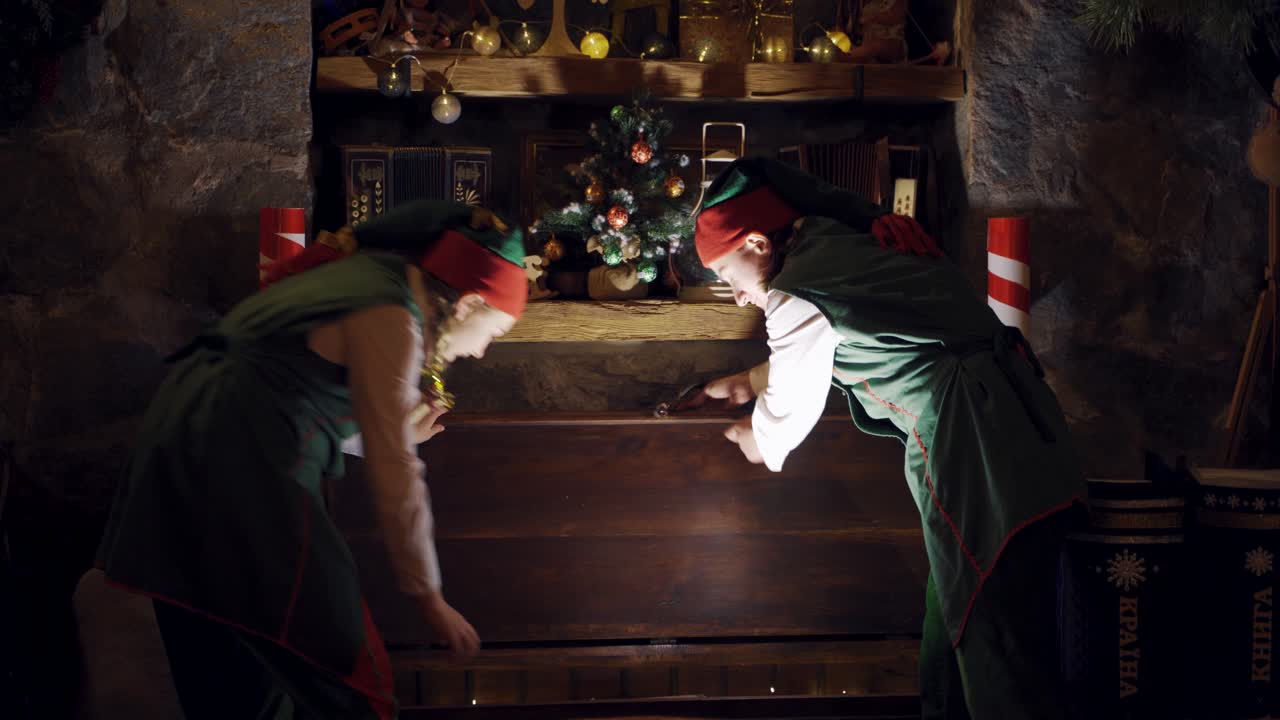 Fairy elves in dark room at Christmas. Excited elves open magic chest and take out a gift indoors. Christmas time.