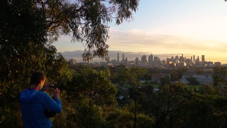 homem usando uma máscara tira fotos do horizonte de uma bela cidade e do pôr do sol