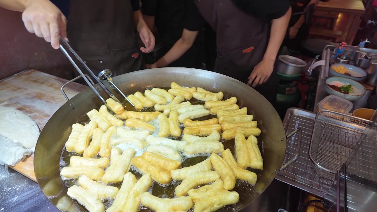 Vendeur de nourriture de rue faisant frire des bâtonnets de pâte Youtiao dans un grand wok