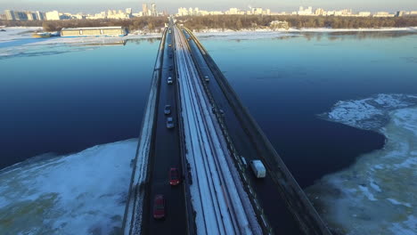 Car-riding-on-highway-bridge-over-winter-river.-Aerial-view-winter-city