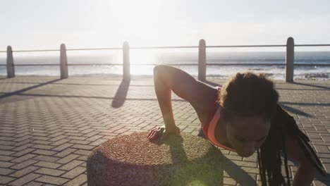 African-american-woman-in-sportswear-doing-press-ups-on-promenade-by-the-sea