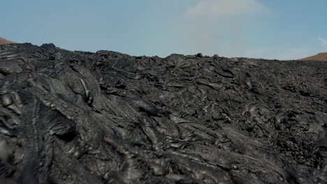 Slide-and-pan-footage-of-dark-stiffed-lava-stream-on-rocky-ground.-Amazing-natural-phenomenon,-layer-of-erupted-magmatic-material.-Fagradalsfjall-volcano.-Iceland,-2021