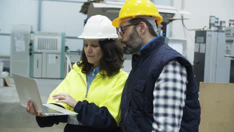 two concentrated technicians standing at factory with laptop