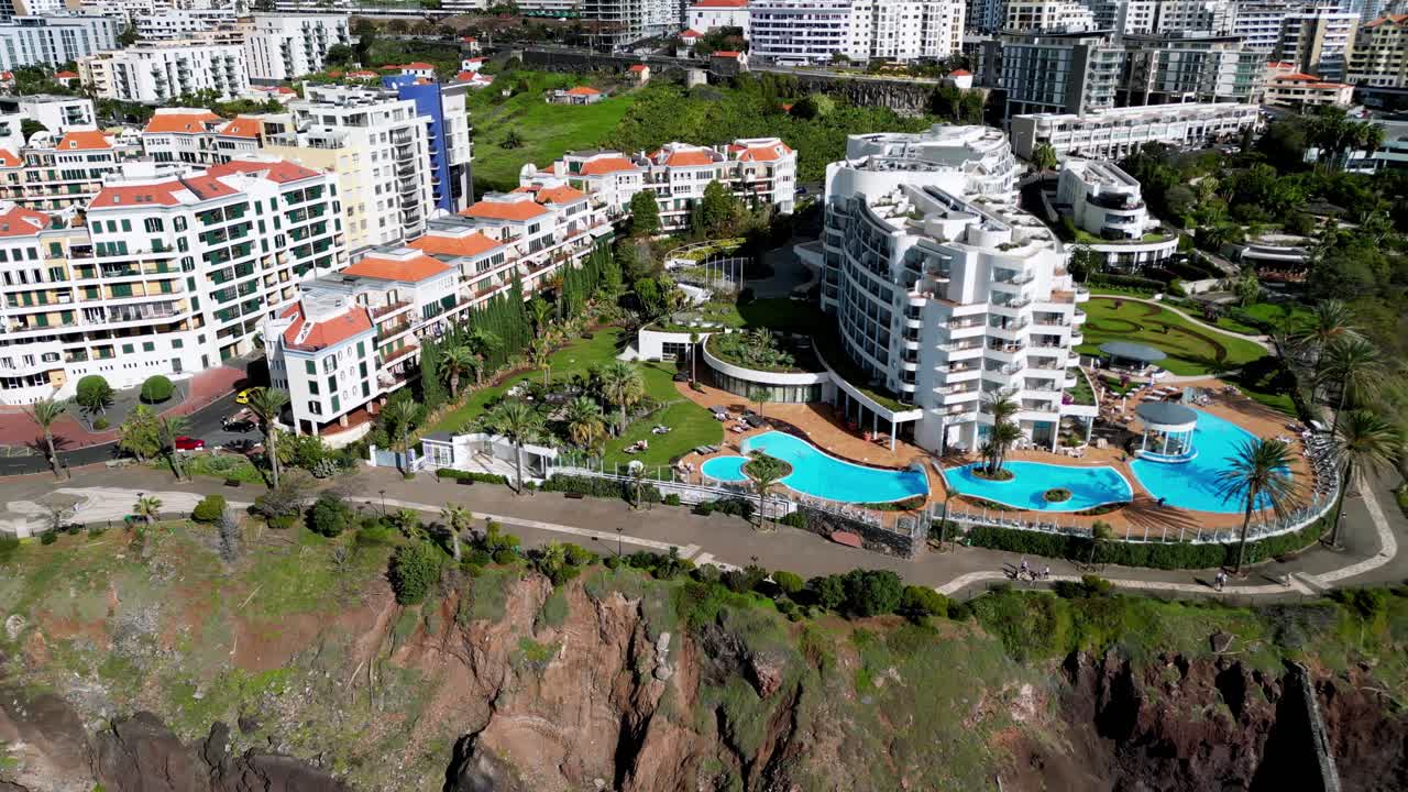 tiro lento de un complejo hotelero familiar en la esquina de una parte idílica de la costa de madeira, piscinas azules brillantes con impresionantes edificios blancos
