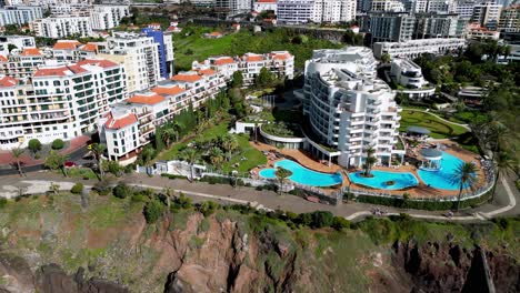 Tiro-Lento-De-Un-Complejo-Hotelero-Familiar-En-La-Esquina-De-Una-Parte-Idílica-De-La-Costa-De-Madeira,-Piscinas-Azules-Brillantes-Con-Impresionantes-Edificios-Blancos