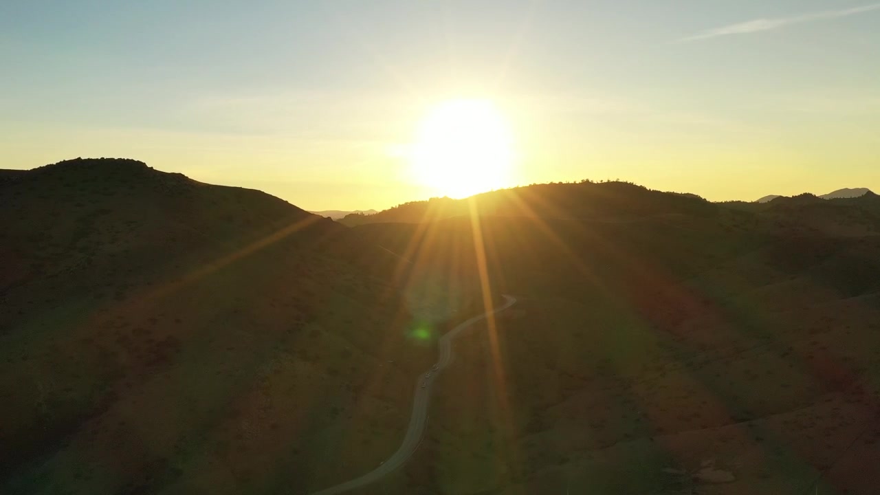 Aerial drone sunset above rugged mountain terrain with winding roads and dramatic golden sun rays in the Middle Atlas Morocco ideal for travel inspirational and documentary projects
