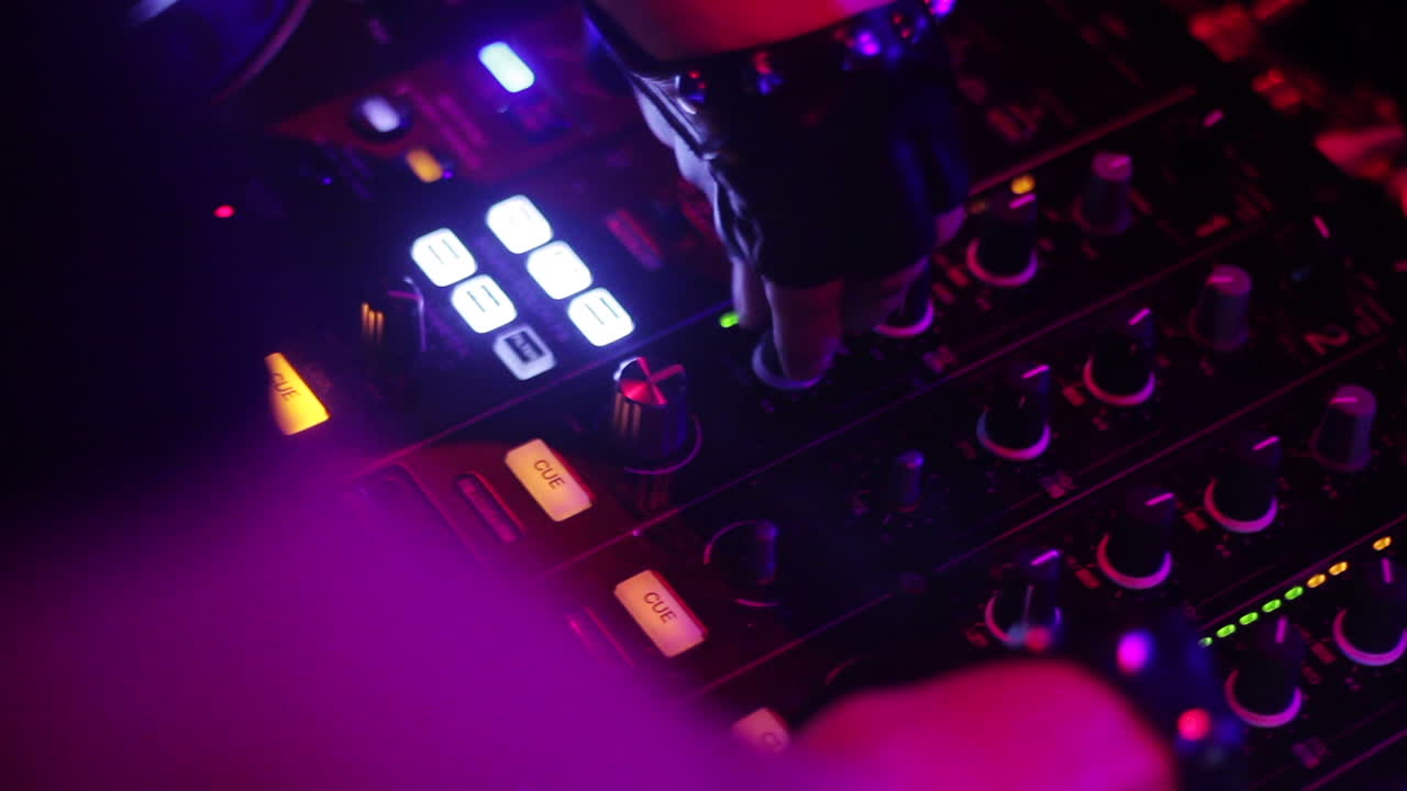 A DJ mixing music on a console with vibrant club lights