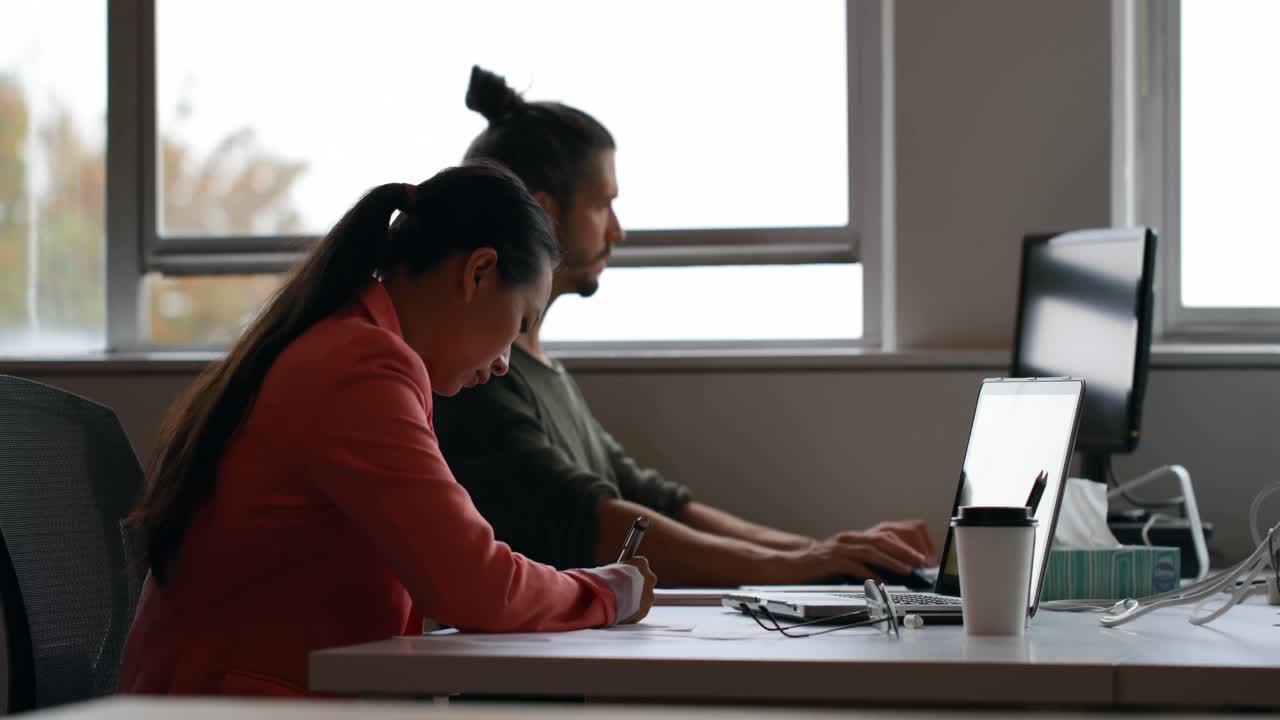 Business colleagues using laptop and writing on diary at desk 4k