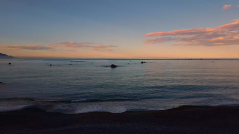 Rising-drone-shot-out-to-sea-at-dusk-with-rocks-in-the-water