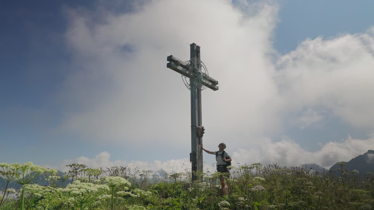 A woman hiking near a large cross on a mountain in Berwang, Austria on a clear day