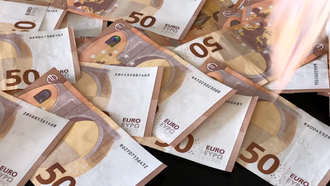muchos billetes de 50 € caen uno a uno sobre una mesa oscura