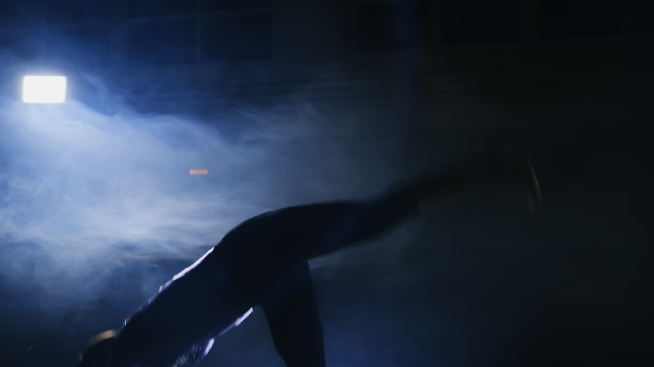 una gimnasta realiza un salto mortal en la alfombra de gimnasia en cámara lenta en la luz de fondo