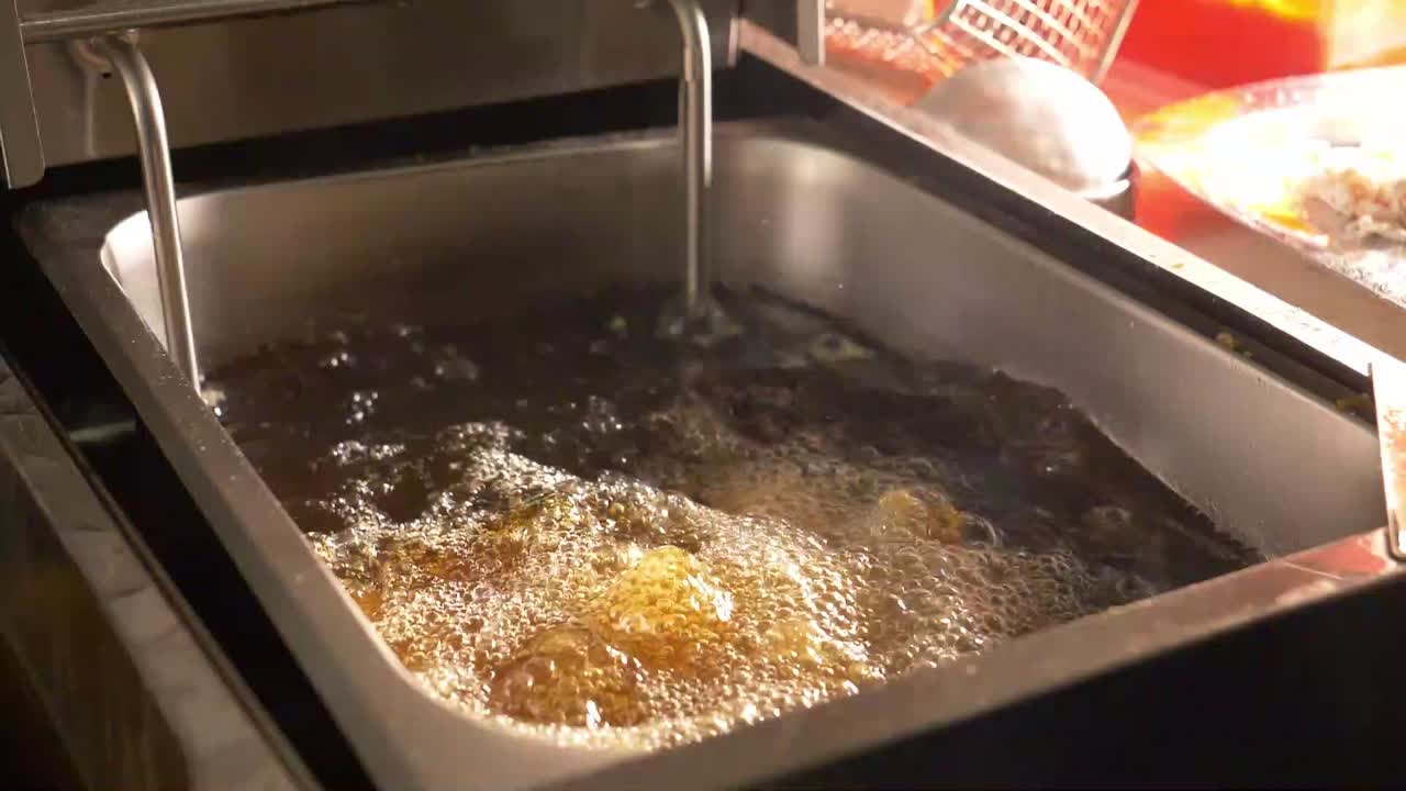 pescado rebozado que se coloca a mano en una freidora de aceite caliente