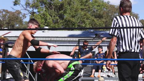 wrestlers compete in an outdoor ring before an audience.