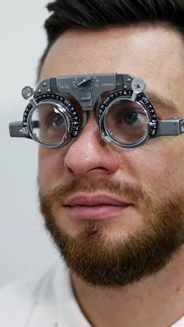 portrait of a young bearded man in testing glasses. patient examining his eyesight with optical trial frame in clinic. ophthalmology concept. vertical video