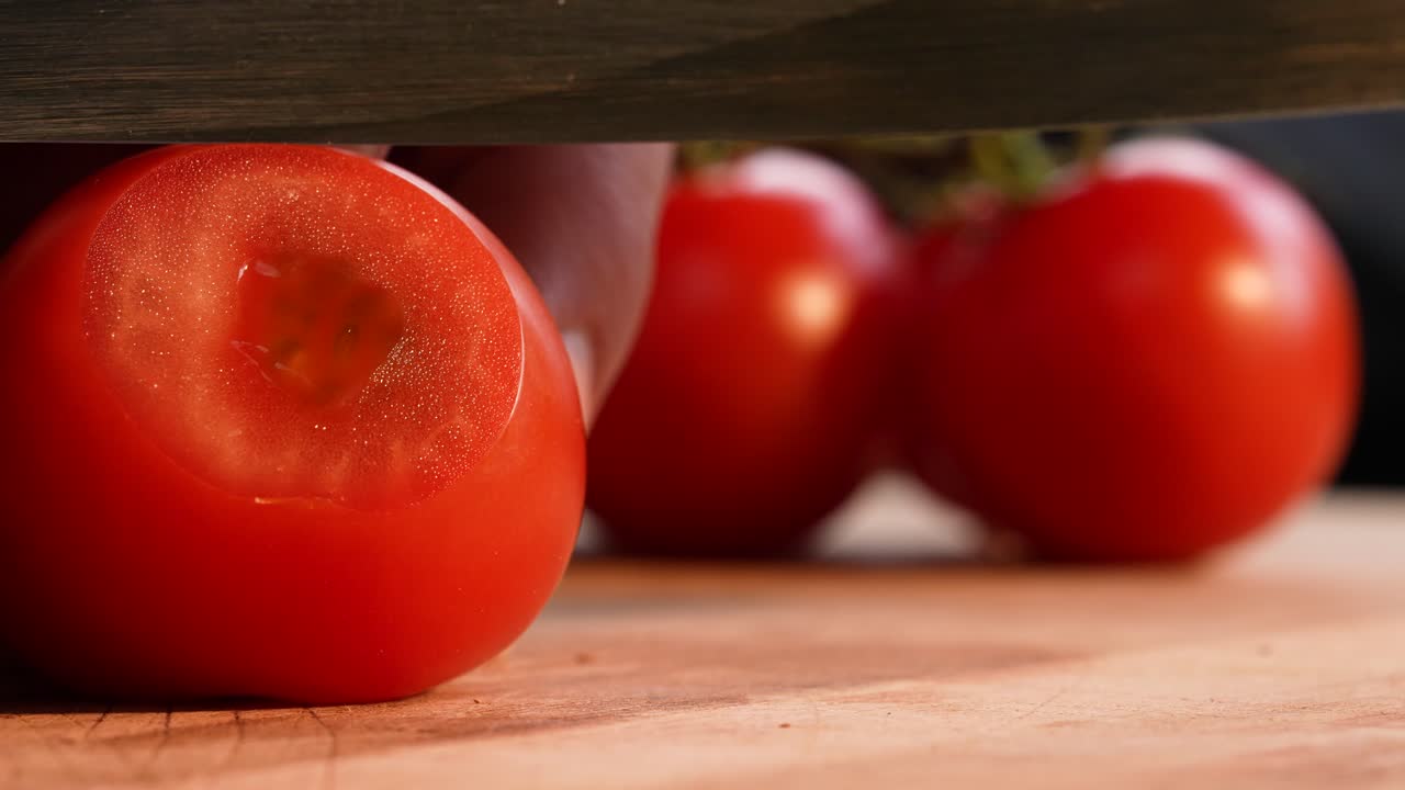 Landscape slow-motion close-up of a tomato being finely shaved into ultra-thin slices using a sharp knife. The gentle blade movement reveals the soft texture and precision of the cut