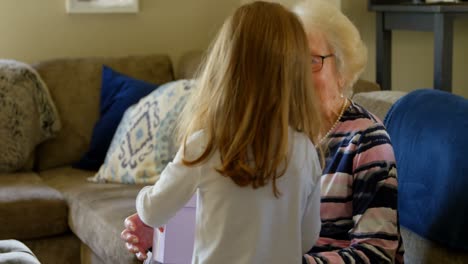 granddaughter giving gift to her grandmother in living room 4k