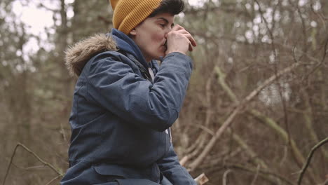 una mujer joven con el pelo corto bebe una bebida caliente en el bosque 1