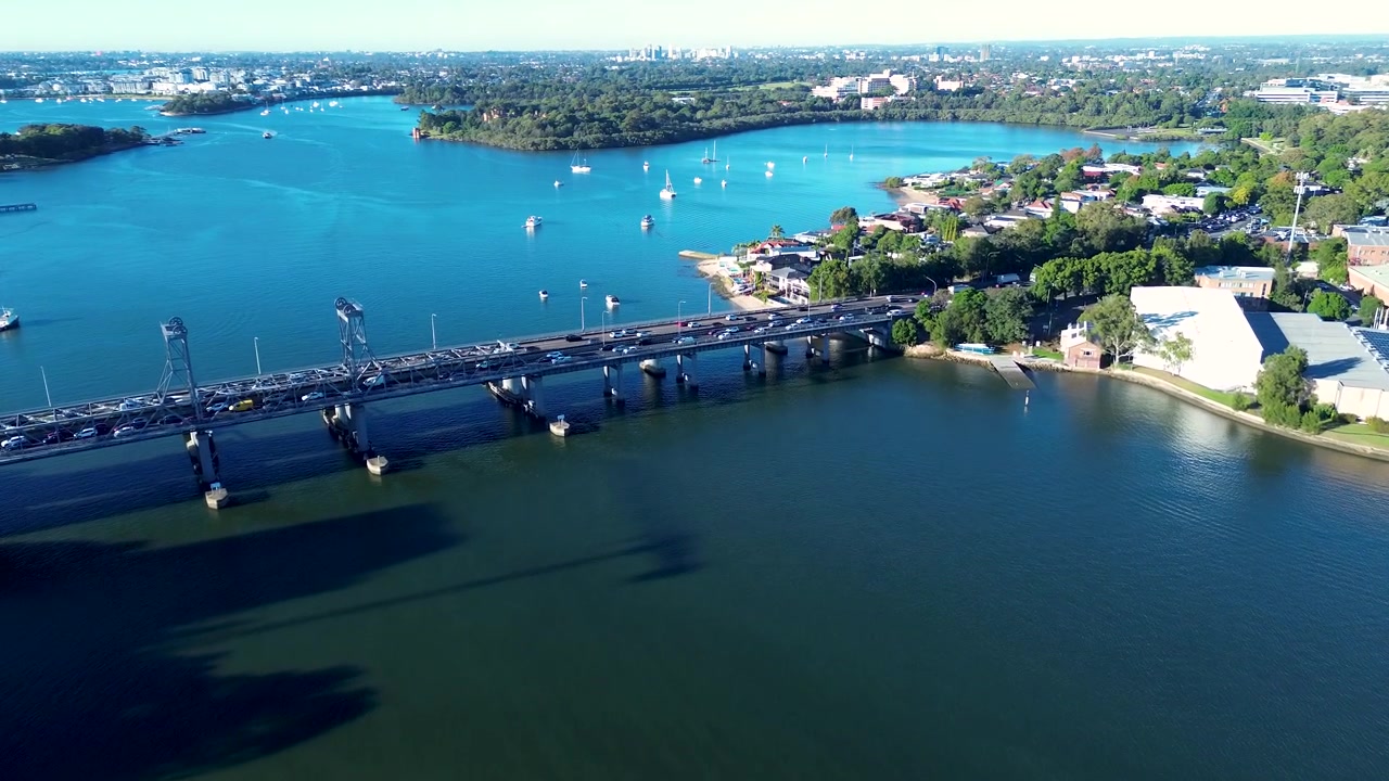 Paesaggio aereo ripreso da drone di veicoli che percorrono la Ryde Bridge Road sopra il fiume Parramatta con la Riserva di Brays Bay sullo sfondo a Meadowbank, Sydney, NSW, Australia, trasporti e infrastrutture.